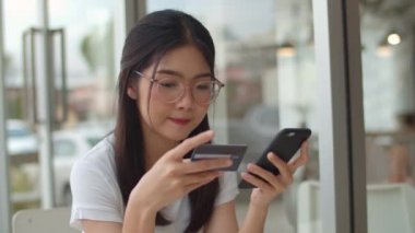 Serbest Asya kadın kahve dükkanında online alışveriş. Genç Asya Kız cep telefonu kullanarak, kredi kartı satın almak ve akşam konsepti açık kafede masada e-ticaret internet satın. Yavaş çekim.