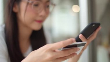 Serbest Asya kadın kahve dükkanında online alışveriş. Genç Asya Kız cep telefonu kullanarak, kredi kartı satın almak ve akşam konsepti açık kafede masada e-ticaret internet satın. Yavaş çekim.