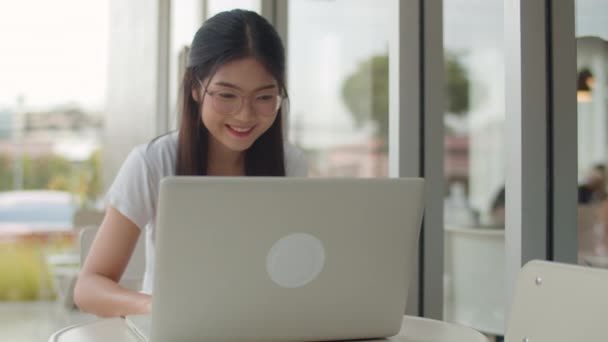 コーヒーショップでラップトップで働くフリーランスのアジア人女性 貿易のためにコンピュータを使用して若いアジアのビジネスガールは 夕方のコンセプトで屋外カフェでテーブル上のインターネット上の電子メール デジタル作業を送信します スローモーション — ストック動画