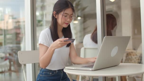 コーヒーショップでフリーランスのアジアの女性オンラインショッピング ノートパソコン クレジットカードを使用する若いアジアの女の子は 夕方のコンセプトの屋外カフェでテーブル上のインターネット上の電子商取引を購入します スローモーション — ストック動画