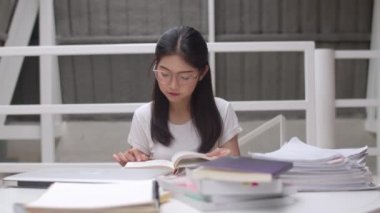 Asyalı öğrenci kadınlar üniversitede kütüphanede kitap okuyor. Üniversite kampüs konseptinde ders masasında bilgi için çok çalışırken genç lisans kız stres yorgun sorun var. Yavaş çekim.