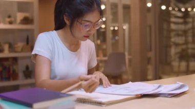 Asyalı öğrenci kadınlar üniversitede kütüphanede kitap okuyor. Genç lisans kız ev ödevi yapmak, ders kitabı okumak, üniversite kampüsünde ders masasında bilgi için çok çalışmak fazla mesai gece. Yavaş çekim.