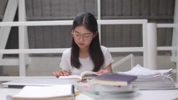 アジアの学生の女性は大学の図書館で本を読みます 若い学部生の女の子は 大学のキャンパスコンセプトの講義デスクで知識を学びながら 疲れた若い女の子が問題を抱えています スローモーション — ストック動画