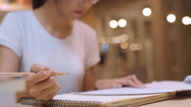 Asyalı öğrenci kadınlar üniversitede kütüphanede kitap okuyor. Genç lisans kız ev ödevi yapmak, ders kitabı okumak, üniversite kampüsünde ders masasında bilgi için çok çalışmak fazla mesai gece. Yavaş çekim.