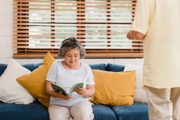 Asiatisk äldre kvinna läser en bok i vardagsrummet hemma. Kinesisk kvinna liggande på soffan när avslappnad hemma. Njuter tid livsstil Senior Kvinna hemma Concept. — Stockfoto