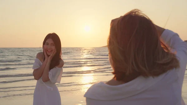 Giovane coppia lesbica asiatica utilizzando fotocamera scattare foto l'un l'altro vicino alla spiaggia. Belle donne lgbt coppia felice momento romantico quando il tramonto in serata. Stile di vita coppia lesbica viaggiare sul concetto di spiaggia . — Foto Stock