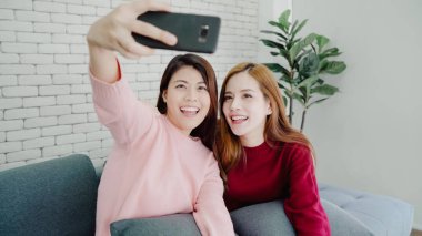 Evde oturma odasında akıllı telefon selfie kullanan lezbiyen Asyalı çift, evde rahat larken kanepede yatarken komik anların tadını çıkarıyor. Yaşam tarzı çift evde kavramı dinlenmek.