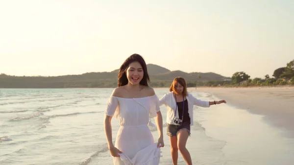 Giovane coppia lesbica asiatica in esecuzione sulla spiaggia. Belle amiche donne felici rilassarsi divertendosi sulla spiaggia vicino al mare quando il tramonto di sera. Stile di vita coppia lesbica viaggiare sul concetto di spiaggia . — Foto Stock