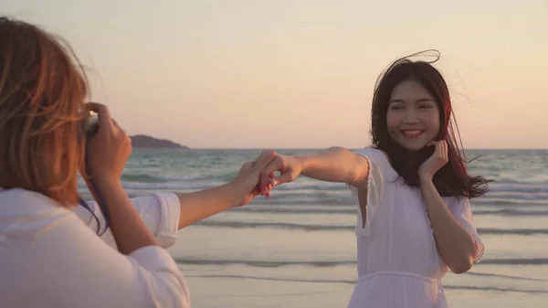 Giovane coppia lesbica asiatica utilizzando fotocamera scattare foto l'un l'altro vicino alla spiaggia. Belle donne lgbt coppia felice momento romantico quando il tramonto in serata. Stile di vita coppia lesbica viaggiare sul concetto di spiaggia . — Foto Stock