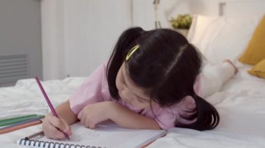 Genç Asyalı kız evde çizim. Asya japon kadın çocuk çocuk dinlenmek eğlenceli gece konsepti yatak odasında yatak odasında uyku, konfor ve sakin yatmadan önce sketchbook karikatür çizin. Yavaş çekim.