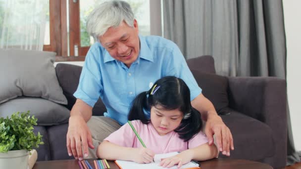 亚洲祖父教孙女画画和在家做作业 高龄的中国人 爷爷开心地放松着 年轻女孩躺在家里的客厅里的桌子上 慢动作 — 图库视频影像