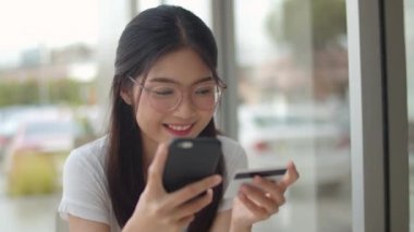 Serbest Asya kadın kahve dükkanında online alışveriş. Genç Asya Kız cep telefonu kullanarak, kredi kartı satın almak ve akşam konsepti açık kafede masada e-ticaret internet satın. Yavaş çekim.