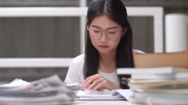 Asyalı öğrenci kadınlar üniversitede kütüphanede kitap okuyor. Genç lisans kız ev ödevi yapmak, ders kitabı okumak, üniversite kampüsünde ders masasında bilgi ve eğitim için çok çalışmak. Yavaş çekim.