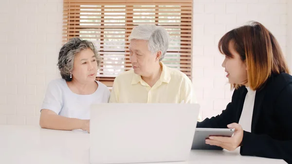 Asia smart female agent offers health insurance for elderly couples by document, tablet and laptop. Aged Asian couple consulting with insurance agent while sitting together with at home. — Stock Photo, Image