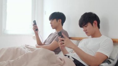 Asyalı Gay çift evde cep telefonu kullanarak. Genç Asyalı Lgbtq erkekler mutlu uyandıktan sonra birlikte dinlenmek, sabah kavramı evde yatak odasında yatakta yatan sosyal medya kontrol edin. Yavaş çekim Shot.