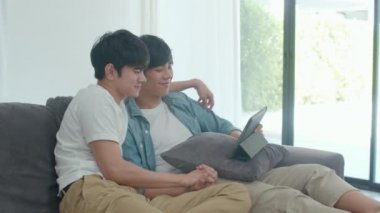 Genç Gay çift evde tablet kullanarak. Asyalı Lgbtq erkekler oturma odası konseptinde kanepe yatarken birlikte internet film izlerken teknolojiyi kullanarak eğlenceli dinlenmek mutlu. Yavaş çekim Shot.