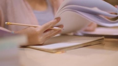 Asyalı öğrenci kadınlar üniversitede kütüphanede kitap okuyor. Genç lisans kız ev ödevi yapmak, ders kitabı okumak, üniversite kampüsünde ders masasında bilgi için çok çalışmak fazla mesai gece. Yavaş çekim.