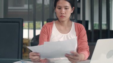 Genç Asyalı hamile kadın laptoptan gelir ve gider kayıtlarını kullanıyor. Baba karısının karnına dokunurken kayıt bütçesi, vergi, mali belge oturma odasında ev konseptinde çalışıyor..