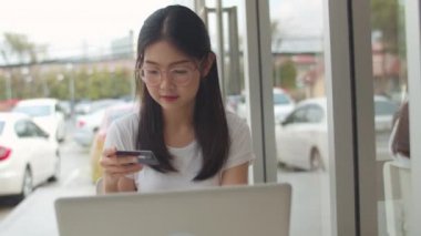 Serbest Asya kadın kahve dükkanında online alışveriş. Genç Asya Kız dizüstü bilgisayar kullanarak, kredi kartı satın almak ve akşam konsepti bir açık hava kafede masada internet üzerinden e-ticaret satın. Yavaş çekim