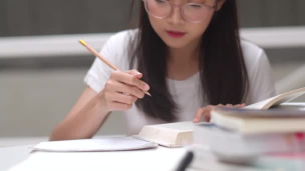 亚洲学生妇女读图书馆的书籍在大学 年轻的本科生女孩做家庭作业 读课本 努力学习知识和教育在课桌在大学校园的概念 — 图库视频影像