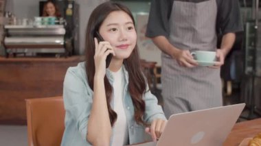 Genç Asyalı serbest kadınlar kahve dükkanında müşterilerle telefonda konuşuyorlar. Asyalı mutlu erkekler garson gri önlük giyer. Kafe veya restoranda çalışan bayan müşterilere sıcak kahve ikram eder..
