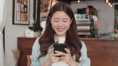 Kafede cep telefonu kullanan serbest Asyalı kadınlar. Genç Japon Asyalı kız akıllı telefon kullanıyor. Kafe konseptinde internette sosyal medyayı kontrol ediyor..