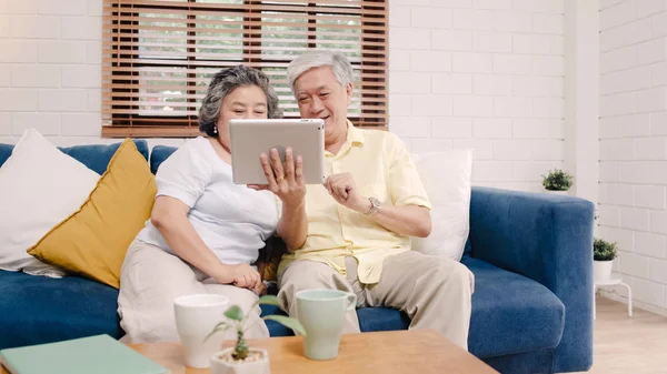 아시아 노인 부부 집에서 거실에서 Tv를 보고 하는 태블릿을 사용 하 여, 몇 집에서 편안한 소파에 누워 있는 동안 사랑 순간을 즐길 수 있습니다. 즐기는 시간 라이프 스타일 수석 가족 홈 개념. — 스톡 사진