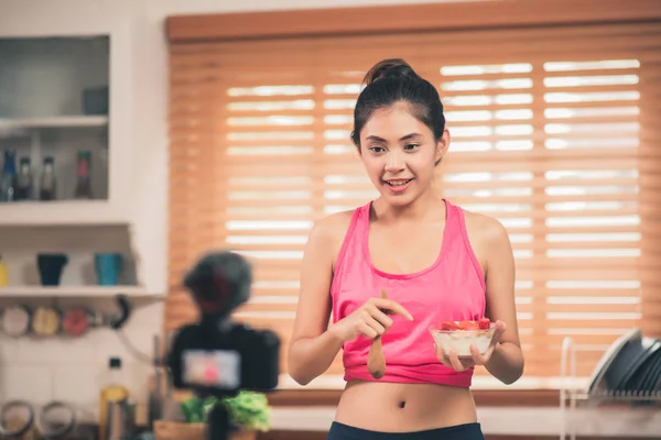 Asiatisk blogger kvinne lage vlog hvordan å diett og gå ned i vekt Ung kvinne bruker kamera opptak når hun spiser yoghurt på kjøkkenet. Livsstilspåvirkende kvinner - sunt begrep . – stockfoto