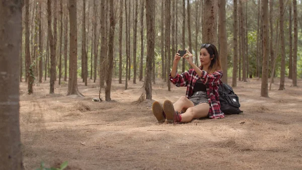 Asiatisk vandrare kvinna vandring i skogen. Young Happy ryggsäck flicka med mobiltelefon ta bilder foto medan resor natur och äventyrsresa, klättra berg i sommarsemester semesterkoncept. — Stockfoto