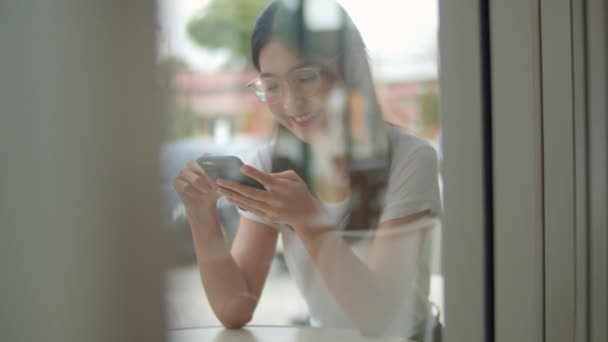 自由职业者在咖啡店使用手机 年轻的亚洲女孩使用智能手机检查社交媒体互联网在户外咖啡馆的桌子上在晚上的概念 慢动作 — 图库视频影像