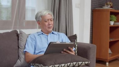 Asyalı son sınıf öğrencileri evde tablet kullanıyor. Asya 'lı üst düzey Çinli erkek ev kavramının oturma odasında kanepede yatarken internette sağlığın nasıl düzeltileceğini araştırıyor..