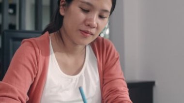 Genç Asyalı hamile kadın karnına ve ailesine not defterine bebek çiziyor. Anne kendini mutlu hissederken, pozitif ve huzurlu gülümserken çocuk evde oturma odasında kendine dikkat ederken..