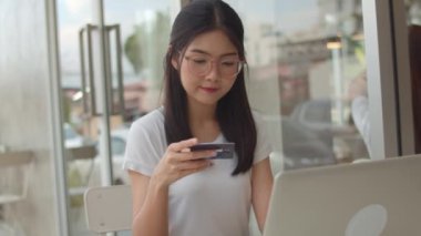 Serbest Asya kadın kahve dükkanında online alışveriş. Genç Asya Kız dizüstü bilgisayar kullanarak, kredi kartı satın almak ve akşam konsepti bir açık hava kafede masada internet üzerinden e-ticaret satın. Yavaş çekim