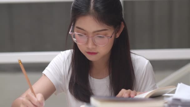 大学の図書館で本を読むアジアの学生の女性 若い学部生の女の子は 宿題を行い 教科書を読み 大学キャンパスのコンセプトで講義デスクで知識と教育のために一生懸命勉強します — ストック動画