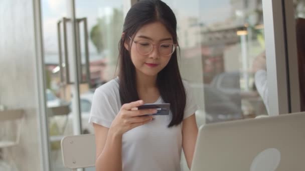 自由职业者亚洲女性在咖啡店网上购物 年轻的亚洲女孩使用笔记本电脑 信用卡购买和购买电子商务在互联网上的桌子上 在户外咖啡馆在晚上的概念 慢动作 — 图库视频影像
