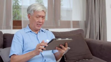 Asyalı son sınıf öğrencileri evde tablet kullanıyor. Asya 'lı üst düzey Çinli erkek ev kavramının oturma odasında kanepede yatarken internette sağlığın nasıl düzeltileceğini araştırıyor..