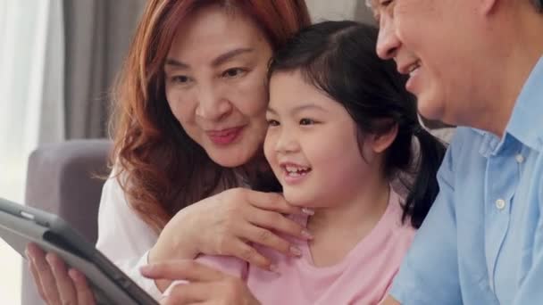 アジア系祖父母と孫娘のビデオ通話 シニア中国人 おじいちゃんとおばあちゃん幸せなです女の子とともに携帯電話ビデオ通話を使用してお父さんとお母さんと話して自宅のリビングルームに横たわって — ストック動画