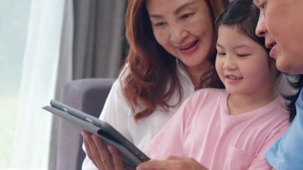 アジアの祖父母と孫娘のビデオ通話は 自宅で呼び出します シニア中国人 おじいちゃん おばあちゃんは リビングルームに横たわっているお父さんとお母さんと話す携帯電話のビデオ通話を使用して女の子と幸せ スローモーション — ストック動画