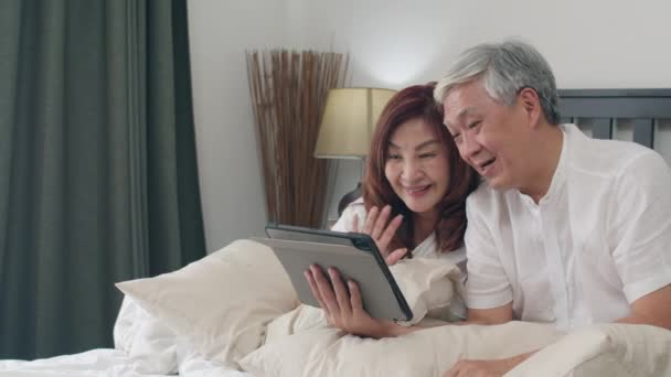 自宅でタブレットを使用してアジアのシニアカップル アジアのシニア中国の祖父母は 朝のコンセプトで自宅の寝室でベッドに横たわっている間 家族の孫の子供たちと話すビデオ通話 スローモーション — ストック動画