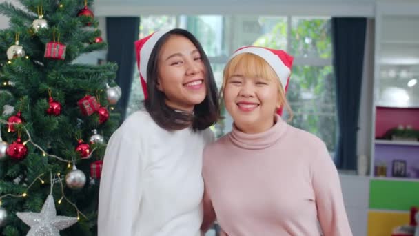 アジアのレズビアンのカップルはクリスマスフェスティバルを祝います Lgbtq女性の十代の若者は 自宅のリビングルームで一緒にクリスマス冬の休日を楽しむカメラを見て幸せな笑顔をリラックスクリスマス帽子を着用 — ストック動画