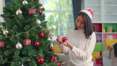 Asyalı kadınlar Noel festivalinde Noel ağacı süsler. Kadın genç mutlu gülümseyerek evde oturma odasında xmas kış tatilleri kutlamak.