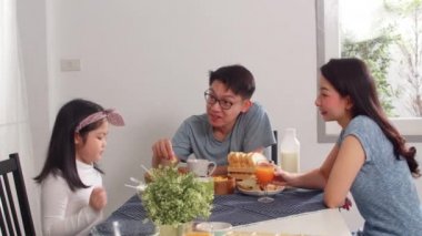 Asyalı Japon ailesi evde kahvaltı yapar. Asyalı anne, baba ve kız birlikte konuşurken mutlu hissediyorlar. Ekmek, mısır gevreği gevreği, mısır gevreği ve sütü sabah mutfakta, masada kasede yiyorlar..