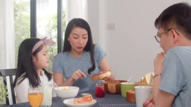 Asyalı Japon ailesi evde kahvaltı yapar. Asyalı mutlu anne kızı için çilek reçeli yapıyor mısır gevreği gevreği ve sütü sabah mutfakta, masada kasede yiyor. Yavaş çekim.