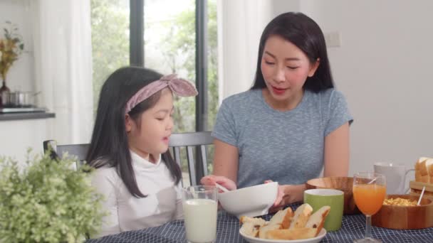 アジア系日本人の家族は家で朝食をとる アジアのお母さんとお父さんと娘は 朝のキッチンのテーブルの上でパン コーンフレークのシリアルとミルクをボウルに入れて食べながら 一緒に幸せな気分で話しています — ストック動画