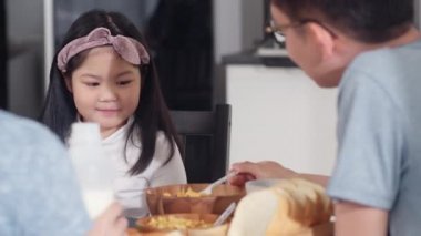 Asyalı Japon ailesi evde kahvaltı yapar. Asyalı anne, baba ve kız birlikte konuşurken mutlu hissediyorlar. Ekmek, mısır gevreği gevreği, mısır gevreği ve sütü sabah mutfakta, masada kasede yiyorlar..