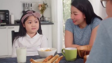 Asyalı Japon ailesi evde kahvaltı yapar. Asyalı anne, baba ve kız birlikte konuşurken mutlu hissediyorlar. Ekmek, mısır gevreği gevreği, mısır gevreği ve sütü sabah mutfakta, masada kasede yiyorlar..