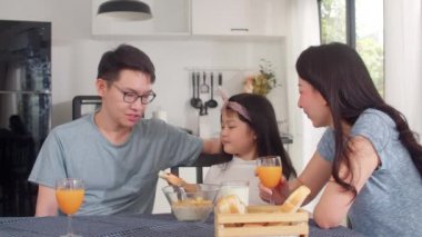 Asyalı Japon ailesi evde kahvaltı yapar. Asyalı mutlu anne kızı için çilek reçeli yapıyor mısır gevreği gevreği ve sütü sabah mutfakta, masada kasede yiyor. Yavaş çekim.