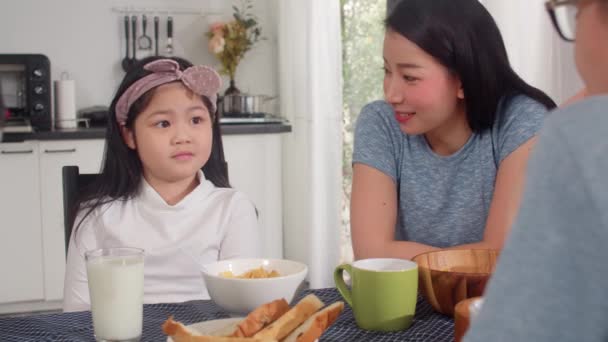 アジア系日本人の家族は家で朝食をとる アジアのお母さんとお父さんと娘は 朝のキッチンのテーブルの上でパン コーンフレークのシリアルとミルクをボウルに入れて食べながら 一緒に幸せな気分で話しています — ストック動画