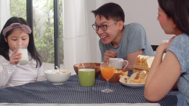 アジア系日本人の家族は家で朝食をとる アジアのお母さんとお父さんと娘は 朝のキッチンのテーブルの上でパン コーンフレークのシリアルとミルクをボウルに入れて食べながら 一緒に幸せな気分で話しています — ストック動画