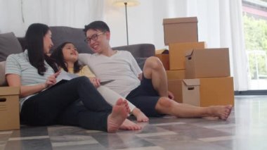 Mutlu Asyalı genç aile sahipleri yeni bir ev satın aldı. Çinli anne, baba ve kız, taşındıktan sonra yeni bir eve taşınmayı dört gözle bekliyor. Kutularla birlikte yerde oturuyorlar..